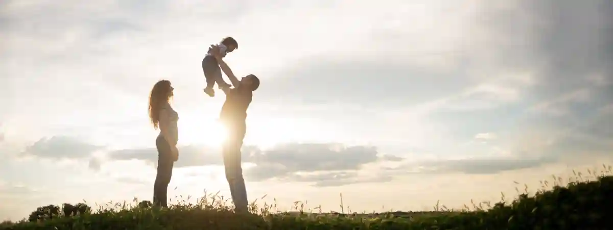 Família ao pôr do sol, com o pai levantando o filho e a mãe ao lado
